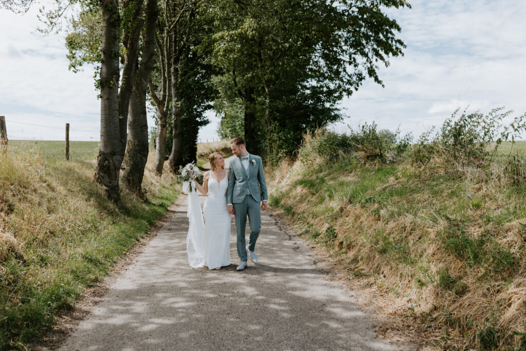 Bruidspaar loopt samen op een weg door de weilanden in Limburg. 